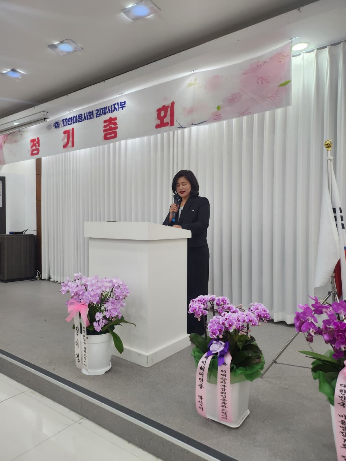 '정기총회' 현수막이 걸린 총회장 — 단상 아래로 축하 난이 놓였다