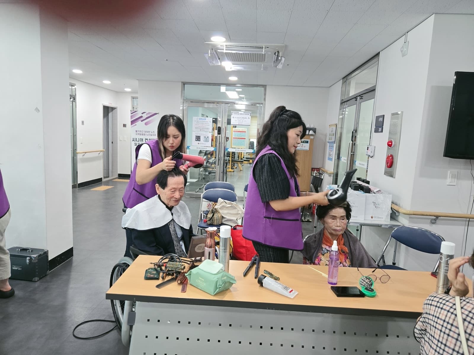 두 명의 회원이 동시에 어르신들의 머리를 손질하고 있다